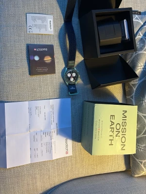 Omega x Swatch Mission on Earth klocka - Säljer en Omega x Swatch Mission on Earth från Bioceramic MoonSwatch Collection. Klockan har blått textilband, mintgrön boett och svart urtavla med vita och röda detaljer. Kommer med originalbox, kvitto och manual.