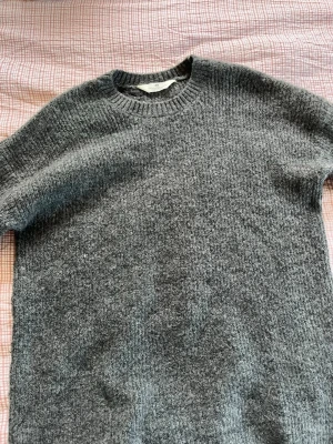 Grå stickad klänning med rund hals - Mysig grå stickad klänning med rund halsringning och ribbstickade muddar. Klänningen har en klassisk rak passform. Materialet känns mjukt och värmande, perfekt för kyligare dagar. Klänningen är ifrån HM och är i storlek 146/152. 