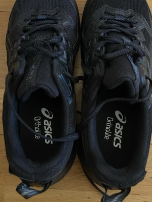 Svarta Asics Gel-Sonoma sneakers - Svarta Asics Gel-Sonoma sneakers med Ortholite-innersula och robust yttersula. Skorna har mesh- och syntetdetaljer, snörning och diskret logga på sidan. Perfekta för dig som gillar sportig stil och vill ha bekväma skor till vardags.