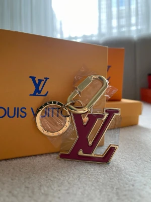  Vuitton LV nyckelring guld/rosa - Snygg nyckelring från  Vuitton med den ikoniska LV-loggan i rosa och guldfärgad metall. Perfekt som accessoar till väskan eller nycklarna. Lyxig och trendig detalj för dig som gillar designeraccessoarer.