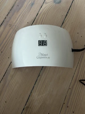 Vit LED UV-lampa för naglar - Vit LED UV-lampa från Nagelgiganten.se med digital display och två knappar för timerinställning (30s/60s). Den är använd men fungerar precis som den ska. Har någon fläck på insidan men de påverkar inte funktionen💕Nypris 500kr