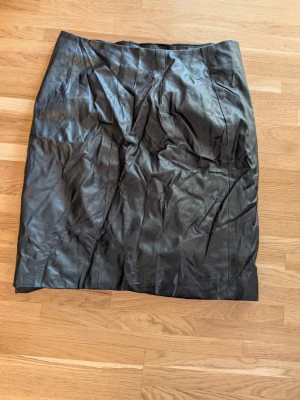 Svart skinnkjol i klassisk modell - Snygg svart kjol i äkta skinn med rak passform. Kjolen har en stilren design utan synliga detaljer och passar perfekt till många olika looks. Materialet är mjukt och följsamt, vilket ger en cool vibe.