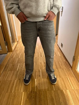 Grå raka jeans i klassisk modell - Säljer ett par grå jeans med rak passform och normal midja. Jeansen har fem fickor, bälteshällor och dragkedjegylf. Materialet är klassisk denim i bomull och färgen är en snygg tvättad grå nyans. Perfekta för en avslappnad och stilren look.