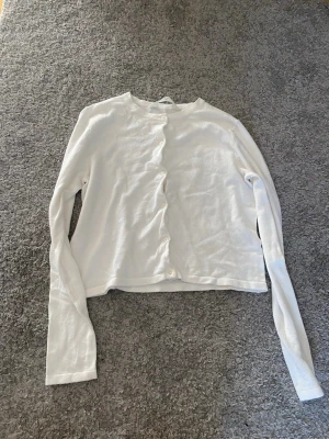 Vit långärmad kofta från H&M - Vit långärmad kofta från H&M med rund halsringning och knäppning framtill. Enkel och stilren design som passar till många olika outfits. Tillverkad i mjukt och lätt material för en bekväm känsla.