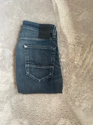 Mörkblå Jack n Jones jeans med slitningar - Snygga mörkblå jeans i slim fit med coola slitningar och klassiska fem fickor. Jeansen har en diskret tvättad look och detaljer i kontrastsömmar. Perfekta för en avslappnad och trendig stil.