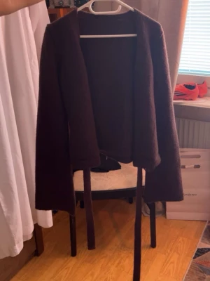 Mörkbrun öppen kofta med knytband - Mysig mörkbrun kofta med långa ärmar och knytband framtill. Koftan har en öppen design utan knappar och är gjord i ett mjukt, stickat material. Perfekt att slänga över en t-shirt eller topp för en avslappnad look.