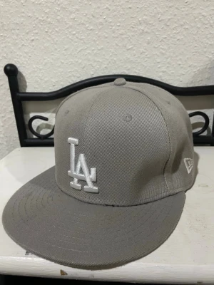 Grå LA Dodgers keps från New Era - Snygg grå keps från New Era med LA Dodgers-logga broderad framtill i vitt och 1988 World Series-märke på sidan. Klassisk flat peak och strukturerad passform. Perfekt accessoar för dig som gillar sportig streetstyle.