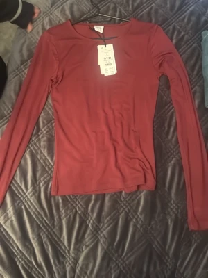 Röd långärmad topp från Gina Tricot - Snygg röd långärmad topp från Gina Tricot med rund halsringning. Tunn och stretchig modell som sitter tight mot kroppen, perfekt att styla med jeans eller kjol. Enkel och stilren design utan mönster eller detaljer.