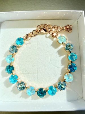Armband med Aqua/turkosa blå stenar  - Snyggt armband med 8mm stora runda stenar i aqua/turkos/azore blue. Infattade i guldfärgad metall. Justerbar kedja med karbinlås. Perfekt för att ge din outfit lite extra färg och glans. Oanvänt. Sista bilden är en inspirationsbild på hur du kan matcha med smycken från Svedbom! 