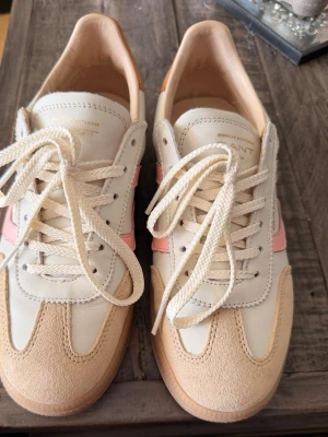Vita och rosa sneakers från Gant - Snygga sneakers från Gant i vitt och beige läder med rosa detaljer på sidorna. Skorna har klassisk låg modell, vita snören och gummisula. Perfekta för dig som gillar stilrena och trendiga sneakers med en touch av färg. Endast använda en gång, kände då att dom var för små för mig.