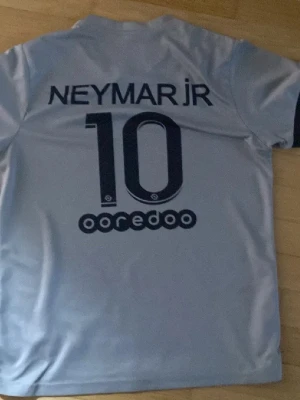 Grå Neymar Jr fotbollströja - Säljer en grå fotbollströja med Neymar Jr och nummer 10 tryckt på ryggen. Tröjan har korta ärmar och är tillverkad i ett lätt och sportigt material som passar perfekt för träning eller match. Snygg design med mörkblå detaljer och logotyp.
