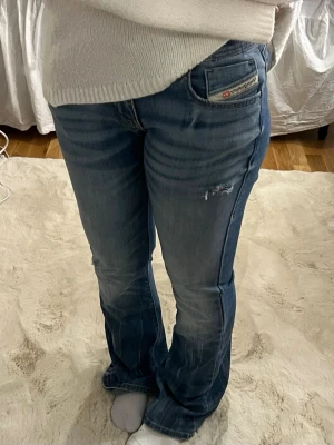 Blå bootcut jeans från Diesel - Säljer ett par blå bootcut jeans från Diesel med slitningar och lätt tvättad look. Jeansen har klassisk femficksmodell och låg midja. Perfekta för dig som gillar en avslappnad och trendig stil.