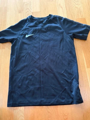 Svart Nike Dri-Fit t-shirt - Svart sportig t-shirt från Nike med Dri-Fit-teknologi som håller dig torr under träningen. Klassisk passform med rund hals och korta ärmar. Diskret Nike-logga på bröstet. Perfekt för gymmet eller löprundan.
