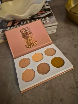 Ögonskuggspalett i varma toner - Säljer en ögonskuggspalett från Juvia's Place med sex nyanser i varma toner. Paletten innehåller både matta och skimrande skuggor i beige, guld, brunt och en unik senapsgul färg. Perfekt för att skapa kreativa och trendiga ögonlooks. Swatchad. Fint skick. 