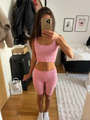 Rosa ribbat set med crop top & shorts - Säljer ett rosa ribbat set med crop top och matchande cykelshorts. Setet är stretchigt och sitter tajt mot kroppen, perfekt för en trendig och bekväm look. Materialet är mjukt och följsamt, och toppen har breda axelband. 