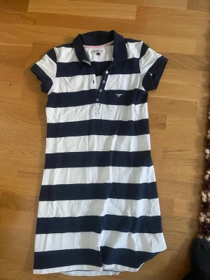 Randig pikéklänning från Hampton Republic - Klassisk pikéklänning från Gant med breda marinblå och vita ränder. Klänningen har korta ärmar, krage och knappar framtill. Perfekt för en sportig och avslappnad stil.