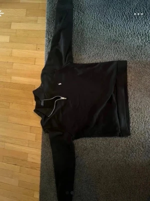 Svart half-zip tröja från Polo Ralph Lauren - Svart långärmad tröja med half-zip och klassisk vit Polo Ralph Lauren-logga broderad på bröstet. Tröjan har ribbade muddar och krage, perfekt för en stilren och avslappnad look.