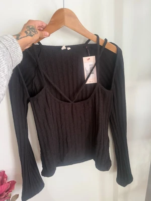 Svart ribbad offshoulder topp - Topp från Nelly med offshoulder-design och smala axelband. 