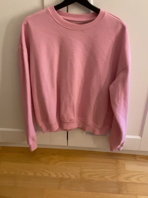 Rosa sweatshirt utan huva - En enkel och stilren rosa sweatshirt med rund halsringning och ribbade muddar vid ärmslut och nederkant. Perfekt för en avslappnad look och lätt att matcha med jeans eller mjukisbyxor.