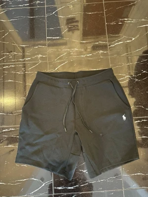 Svarta shorts från Polo Ralph Lauren - Svarta shorts från Polo Ralph Lauren med klassisk broderad logga i vitt på vänster ben. Modellen har snörning i midjan och två sidofickor. Perfekta för en avslappnad stil och tillverkade i mjuk bomull.