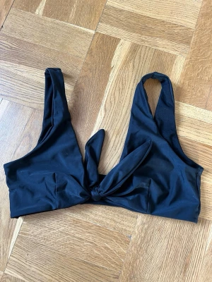 Svart bikiniset Nelly - Svart bikiniöverdel med breda axelband och knyt framtill. Matchande enkel underdel i brazilian-model.