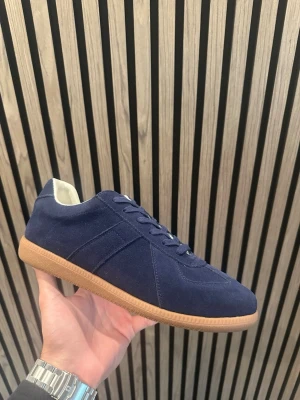 Mörkblå sneakers maison - Stilrena mörkblå sneakers i mocka med klassisk låg profil och ljusbrun gummisula. Skorna har ton-i-ton snörning och vit insida för en clean look. Perfekta för dig som gillar minimalistisk och tidlös stil.