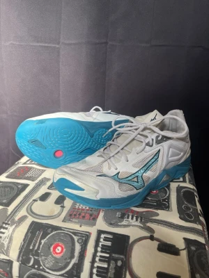 Vita och blå Mizuno träningsskor - Mizuno wave momentum 3 low. Fräscha träningsskor från Mizuno i vitt med blå detaljer och blå sula. Skorna har meshpaneler för extra andningsförmåga, snörning och en sportig vibe. Mizuno-loggan syns tydligt på sidan och sulan har coola mönster för bra grepp.
