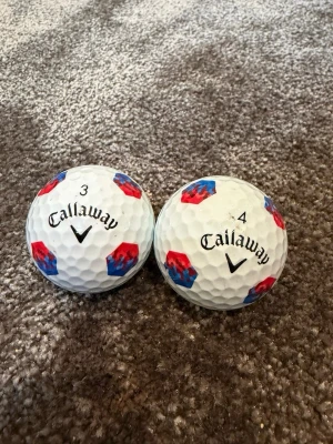 Callaway golfbollar med mönster - Två vita golfbollar från Callaway med unikt rött och blått hexagonmönster. Bollarna har siffrorna 3 och 4 tryckta på sig och klassisk Callaway-logga. Perfekta för dig som vill sticka ut på golfbanan.
