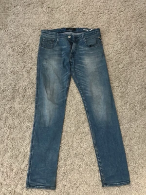 Blå slim fit jeans från Replay - Snygga blå slim fit jeans från Replay, modell Anbass. Jeansen har klassisk femficksdesign, dragkedjegylf och lätt slitna detaljer framtill för en cool look. Perfekta för dig som gillar en modern och avslappnad stil.