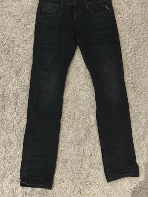 Svarta Replay Hyperflex jeans - Säljer ett par svarta Replay Hyperflex jeans, modell Anbass. Jeansen har slim fit passform, klassisk femficksdesign och stretchigt material för extra komfort. Snygga detaljer och diskret tvättad look gör dem perfekta till alla outfits.
