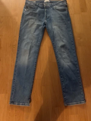 Blå raka jeans i klassisk modell - Säljer ett par blå jeans med rak passform och fem fickor. Jeansen har en klassisk ljus tvätt och är tillverkade i denim. Perfekta för en avslappnad och stilren look. STORLEK W30 L30