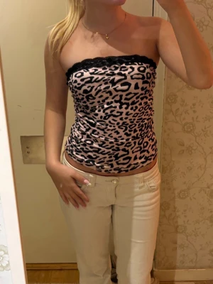 Leopardmönstrad tubtopp - Snygg ljusrosa tubtopp med svart leopardmönster och spetskant upptill. Toppen är figurnära och axelbandslös, perfekt för dig som vill sticka ut med en trendig look. Storleken står tyvärr inte i då lappen är avklippt men skulle gissa på xs/s!💗🐆