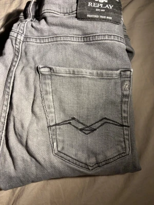 Grå jeans från Replay - Snygga grå jeans från Replay med raka ben och klassisk femficksdesign. Jeansen har en diskret tvättad look och coola detaljer på bakfickan. Perfekta för en avslappnad stil och lätta att matcha med det mesta. Materialet är mjukt och bekvämt denim.