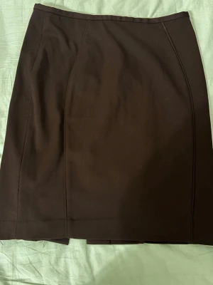 Mörkbrun klassisk pennkjol - En svart, stilren pennkjol med enkel design och diskreta sömmar. Kjolen har en rak passform och är perfekt för en clean och tidlös look. Passar till många olika outfits och är ett måste i garderoben.