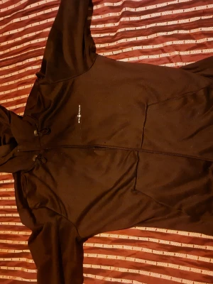 Svart hoodie från sailrqsing - Svart hoodie från saiörasing med dragkedja framtill och justerbar huva. Tillverkad i ett mjukt material som känns skönt mot huden. Diskret logga på bröstet och praktiska fickor på sidorna. Perfekt för en avslappnad och sportig stil.