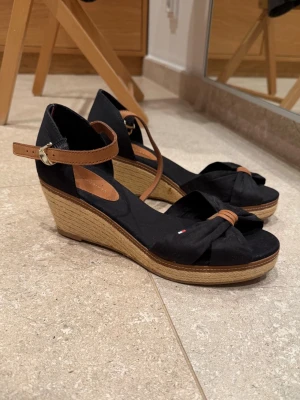 Svarta sandaletter - Svarta sandaletter från Tommy Hilfiger. Använda ett fåtal gånger, samlat damm i garderoben. Klistret i klacken har åldrats och gett pyttesmå missfärgningar, men som lätt skrapas bort. I övrigt mycket fina. Säljs i befintligt skick. 
