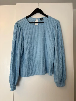 Ljusblå strukturerad blus - Ljusblå blus med långärmad design och rund halsringning. Blusen har ett strukturerat tyg med vertikala ränder och en knapp i nacken som skapar en liten öppning bak. 