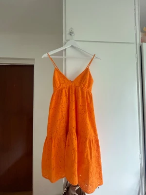 Orange broderad sommarklänning - Snygg orange klänning med tunna axelband och broderade hålmönster. 