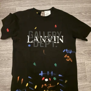 Lanvin Svart t-shirt från Gallery Dept. - OBS! läs till slutet. Snygg svart t-shirt från Gallery Dept. med färgglada penseldrag och texten 'LANVIN' tryckt på framsidan. Perfekt för dig som vill ha en unik och konstnärlig stil. Kortärmad och i en skön passform. Obs prislappen finns ej kvar!