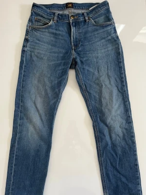 Lee jeans - Säljer ett par klassiska blå jeans från Lee med rak passform och fem fickor. Jeansen har snygga slitningar och kontrastsömmar, samt en Lee-lapp bak i midjan. Perfekta till en avslappnad stil och tillverkade i slitstarkt denimtyg. Trendiga