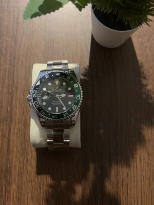 Klocka  - Säljer snygga herrklockor i rostfritt stål. Den ena har svart och grön vridbar bezel och länkarmband, den andra har svart urtavla med datum och räfflad bezel. Båda har klassisk design och passar perfekt till dig som gillar exklusiva accessoarer.