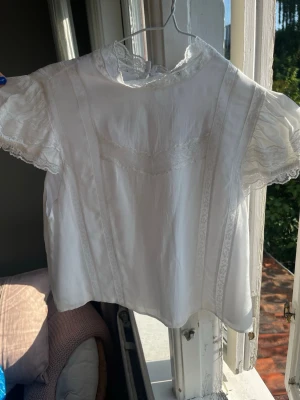 Vit blus med spetsdetaljer från H&M - Söt vit blus från H&M Divided med spetsdetaljer längs ärmar och framstycke. Blusen har korta puffärmar och rund halsringning. Tillverkad i mjuk viskos som ger ett luftigt och bekvämt intryck. Perfekt för en romantisk och trendig look.