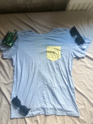 Ljusblå t-shirt från polo Ralph Lauren  - Säljer en ljusblå t-shirt med en gul bröstficka som har en broderad polo Ralph lauren logg. T-shirten har rund hals och korta ärmar. Perfekt för dig som gillar en enkel men ändå unik stil. Pris kan diskuteras.