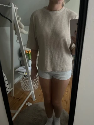 Beige ribbad topp med halvärm - Säljer en beige ribbad topp med rund hals och halvärm. Toppen har en loose passform och är tillverkad i ett mjukt material som känns skönt mot huden. Perfekt för en avslappnad och stilren look.