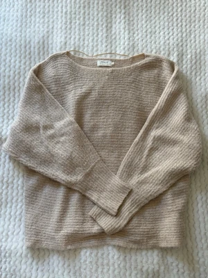 Beige stickad tröja från ONLY - Mysig beige stickad tröja från ONLY med rund halsringning och långa ärmar. Tröjan har en avslappnad passform och ribbade muddar vid ärmslut och nederkant. Perfekt för lager på lager och enkel att matcha med jeans eller kjol.
