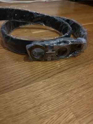 Svart Ferragamo Bälte Lyche Design - Snyggt svart skärp från Ferragamo med ikoniskt silverfärgat spänne. Skärpet är gjort i skinn och har en stilren design som passar till många olika outfits. Perfekt accessoar för att lyfta din look. Storleken är 105 cm.
