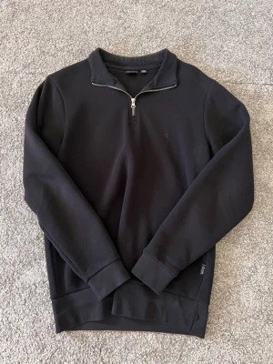 Svart halvzip tröja från Only & Sons - Svart långärmad tröja från Only & Sons med halv dragkedja vid halsen. Tillverkad i mjukt sweatshirtmaterial och har ribbade muddar vid ärmslut och nederkant. Enkel och stilren design som passar till det mesta.