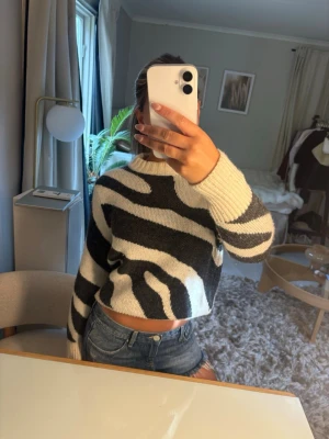 Zebramönstrad stickad crop tröja - Säljer en stickad crop tröja med zebramönster i svart och vitt. Tröjan har rund halsringning, långa ärmar och är gjord i ett mjukt material som känns skönt mot huden. 