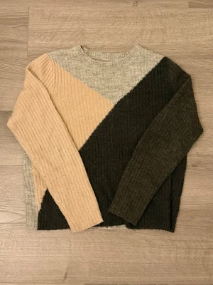 Stickad tröja i blockfärger S - Snygg stickad tröja med ribbad struktur i blockfärger: beige, ljusgrå och mörkbrun. Tröjan har rund halsringning och långa ärmar. Defekter förekommer: nopprig (går att få bort med noppborttagare)
