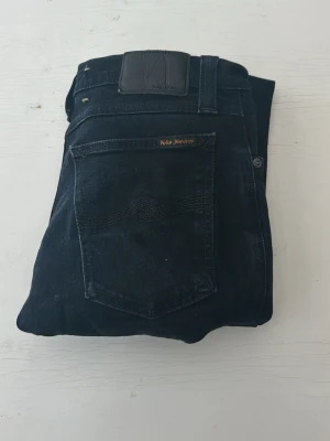 Svarta jeans från Nudie Jeans - Snygga svarta jeans från Nudie Jeans med klassisk femficksmodell och raka ben. Jeansen har subtila sömdetaljer på bakfickan och är tillverkade i mjuk denim. Perfekta för dig som gillar en stilren och tidlös look.